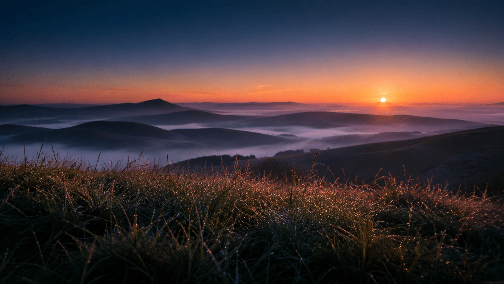 Dawn breaking over layered misty ridgelines, the sun cresting the horizon